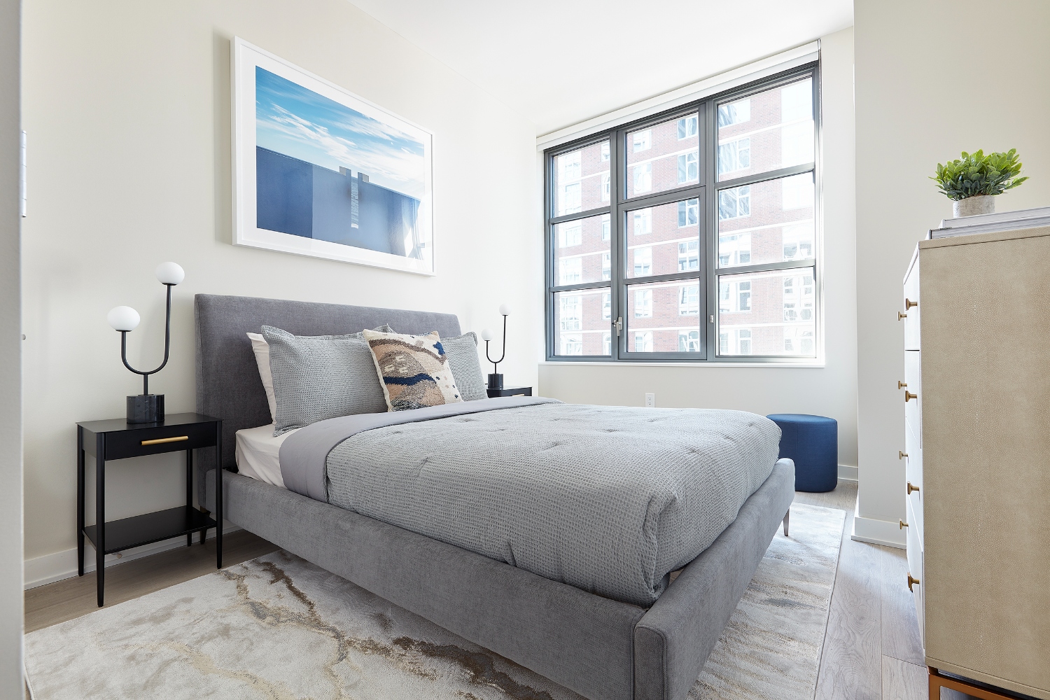 A modern, minimalistic bedroom with a grey bed and large window.
