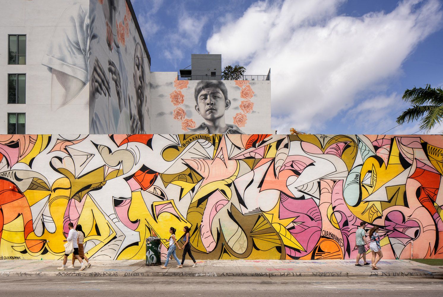 Colorful street mural with abstract designs and people walking nearby.