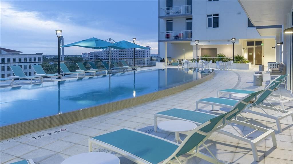 Rooftop pool area with lounge chairs and umbrellas at dusk.