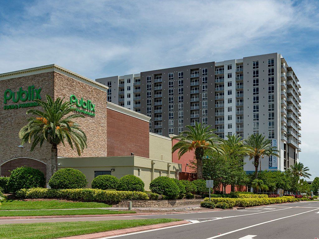 Modern building alongside a commercial structure with palm trees and landscaping.