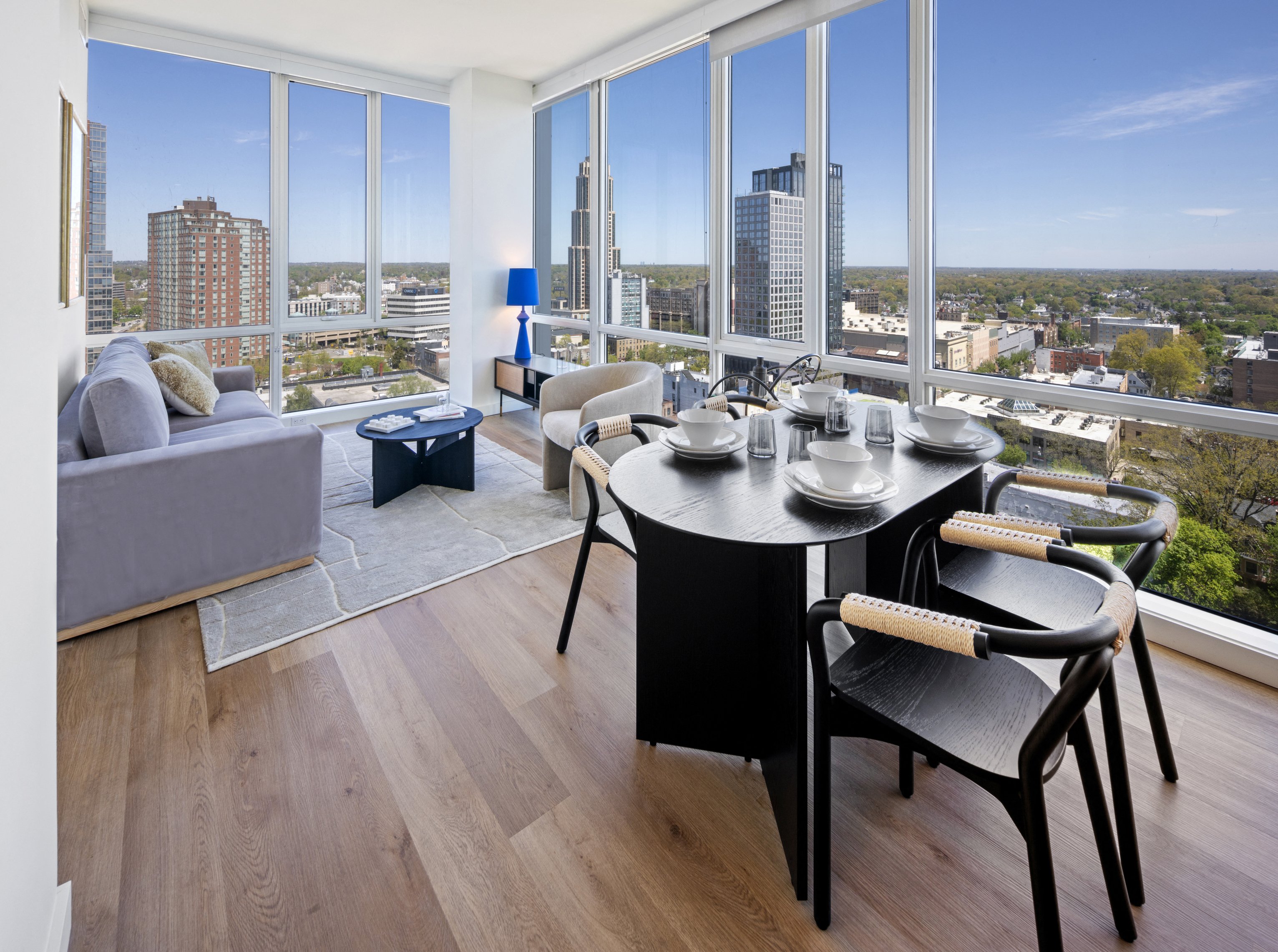 Modern apartment interior with a dining area and large windows offering city views.