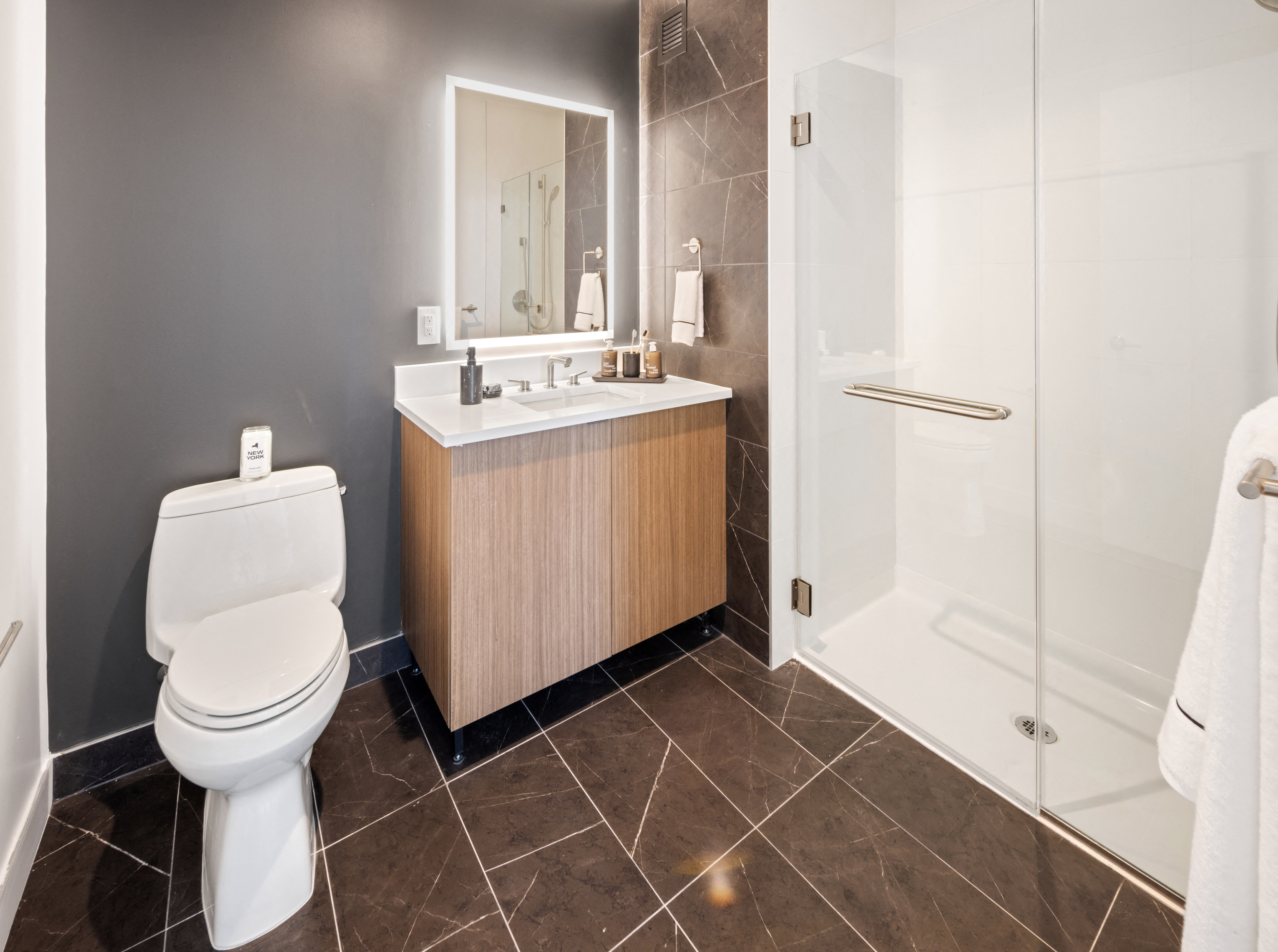 Modern bathroom featuring a toilet, vanity, mirror, and glass shower.