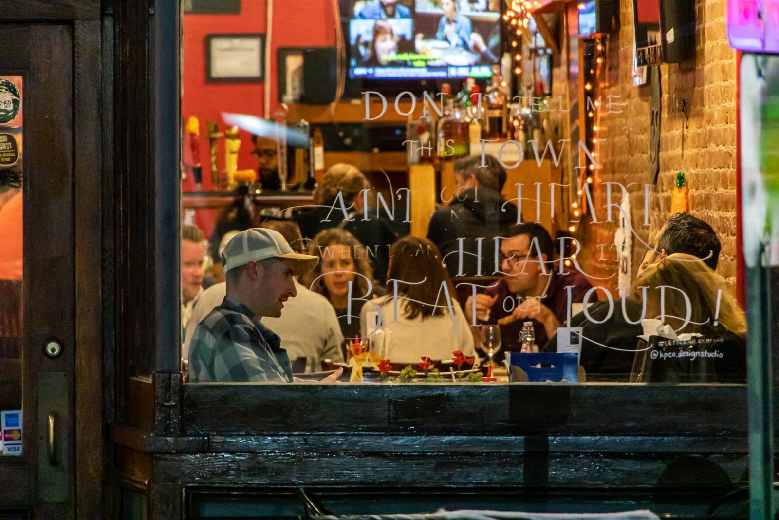 A busy restaurant scene viewed through a window, with patrons dining and chatting.