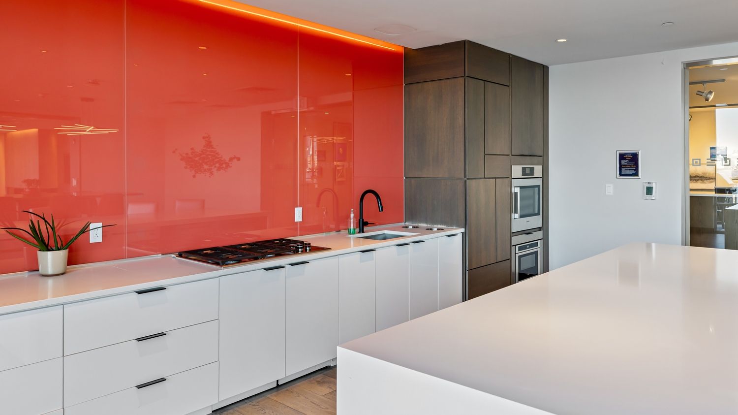 Modern kitchen with orange accent wall, white cabinets, and a sleek countertop.