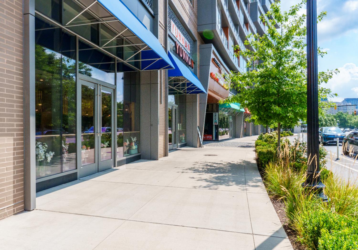 Outdoor shopping area with trees and storefronts under bright blue sky.