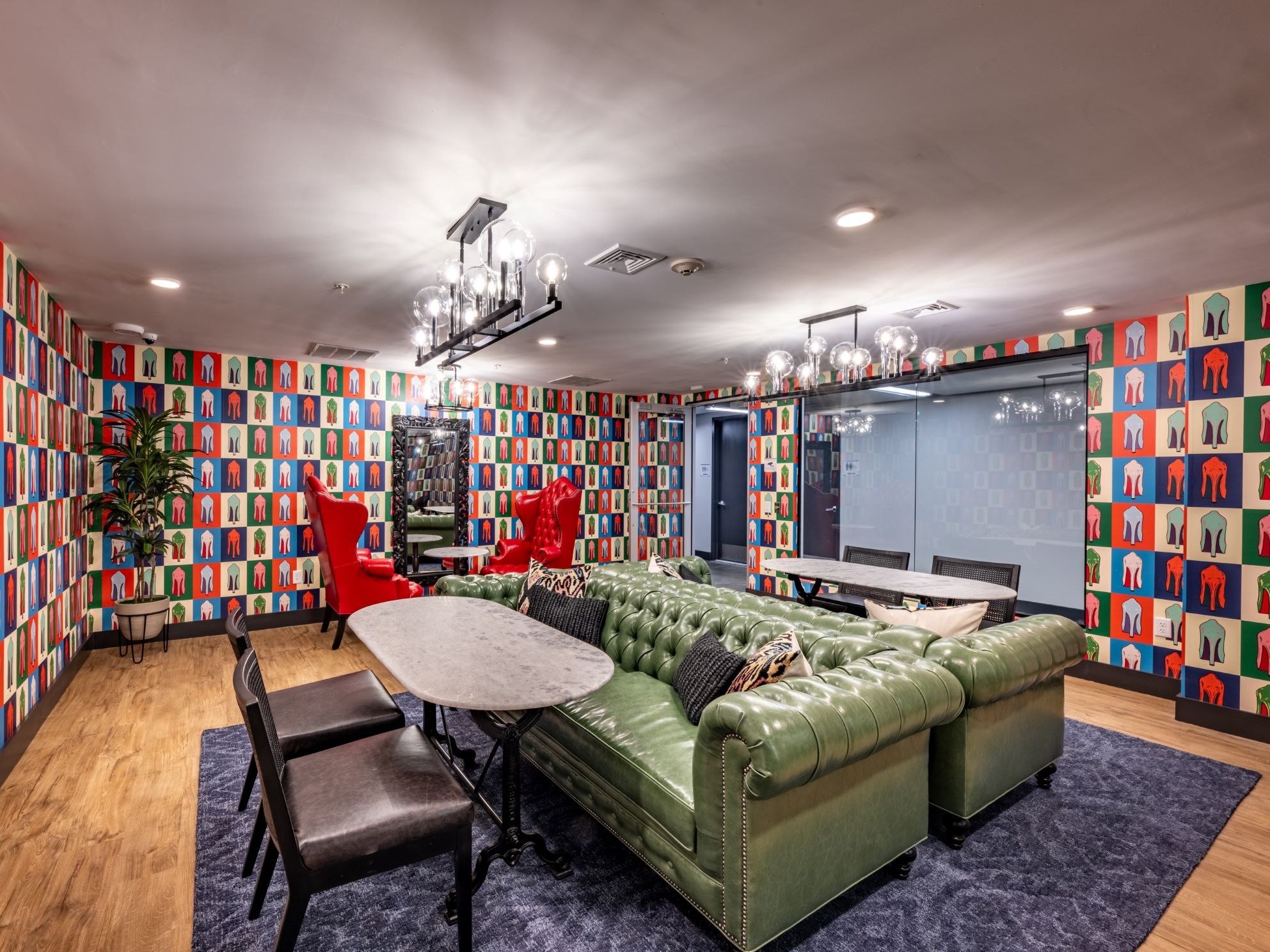 Modern lounge with green sofa, red chairs, and colorful book-patterned walls.
