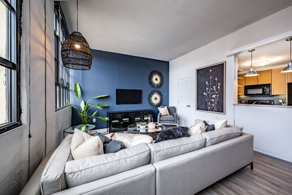 Modern living room with a gray couch, blue accent wall, and open kitchen area.