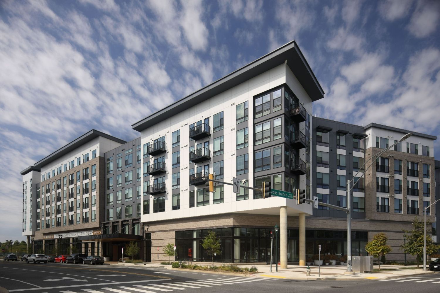 Modern multi-story apartment building with large windows and balconies under a cloudy sky.
