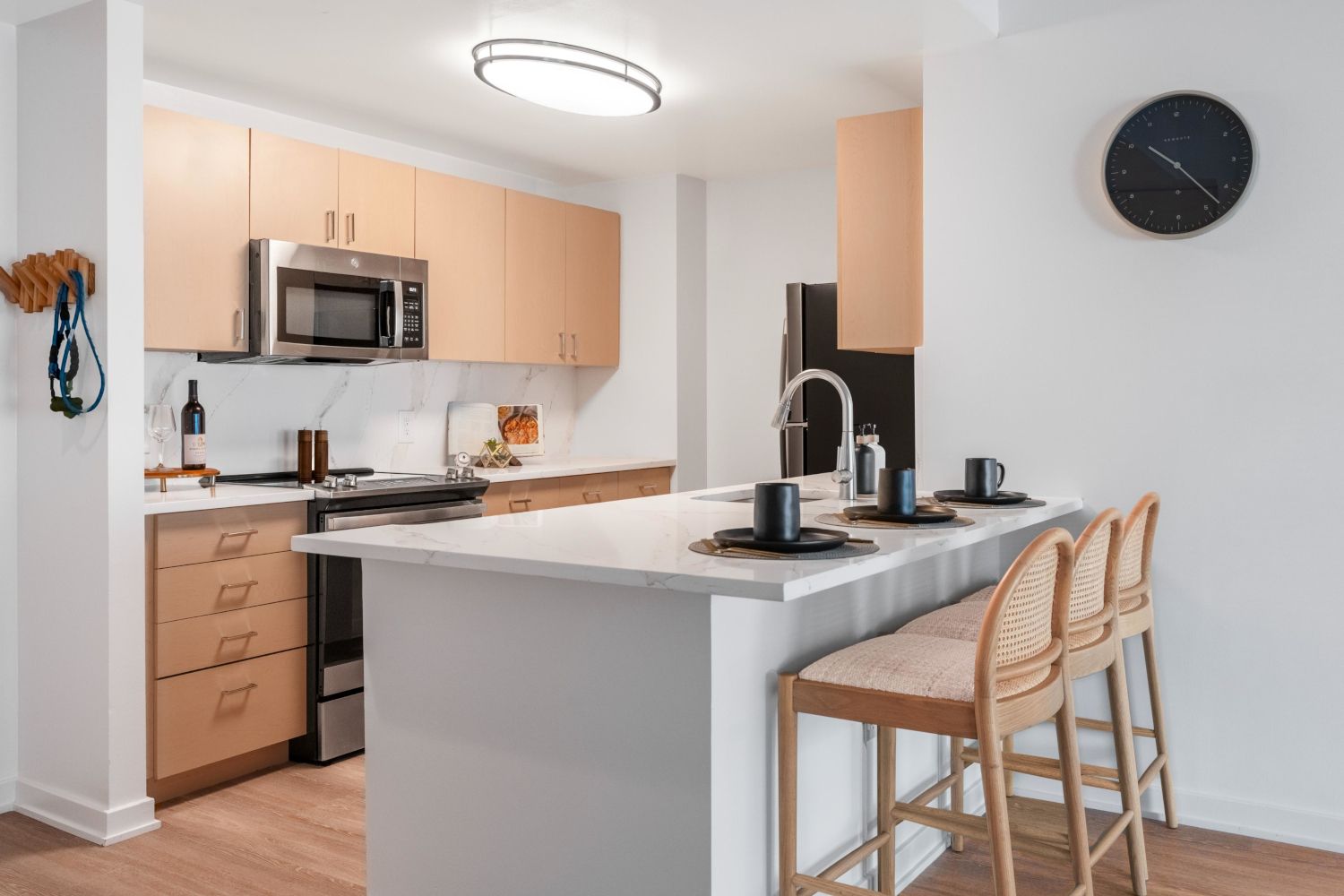 Modern kitchen with light wood cabinets, stainless steel appliances, and bar seating.