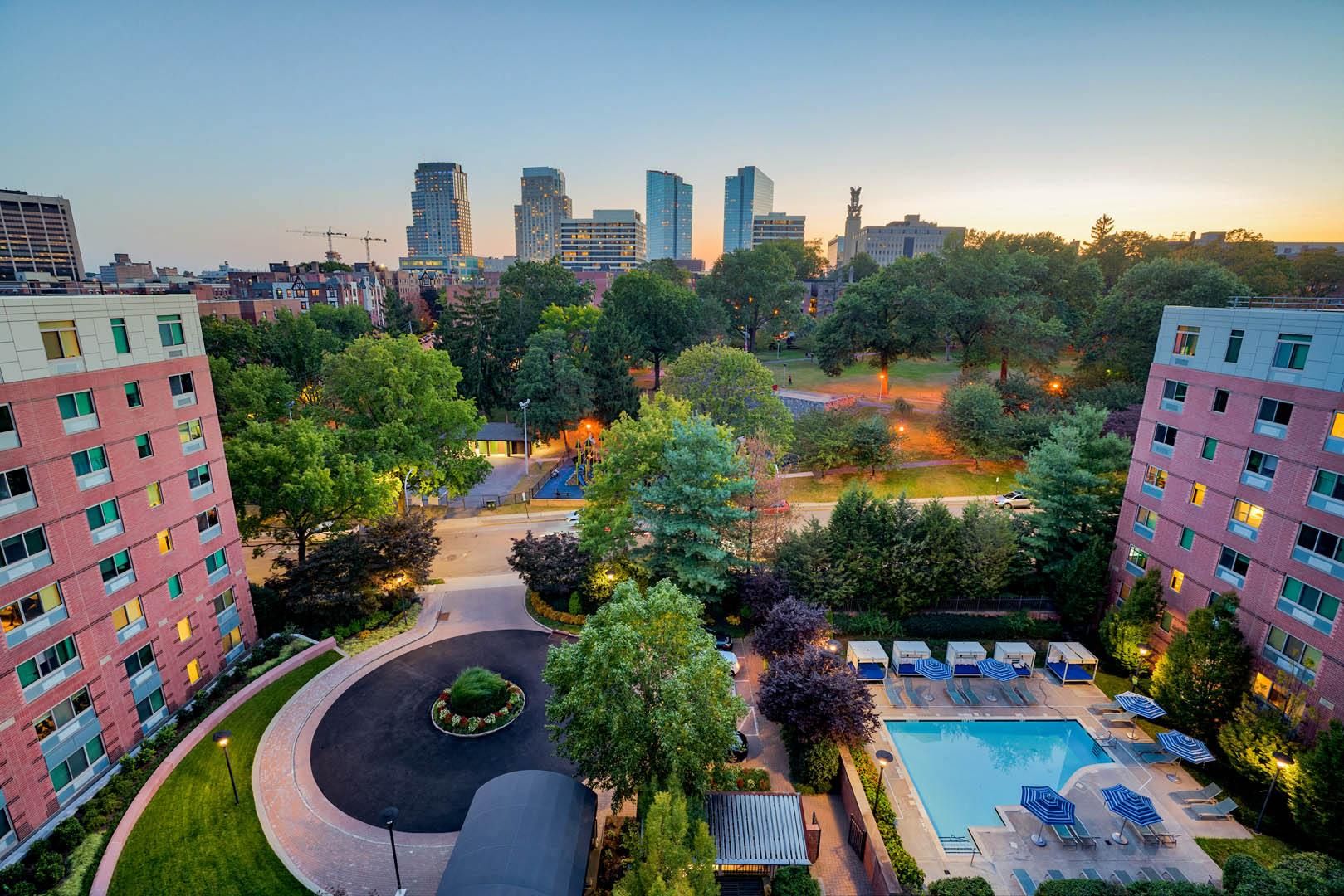 City skyline at sunset with residential buildings and a pool in a lush park.