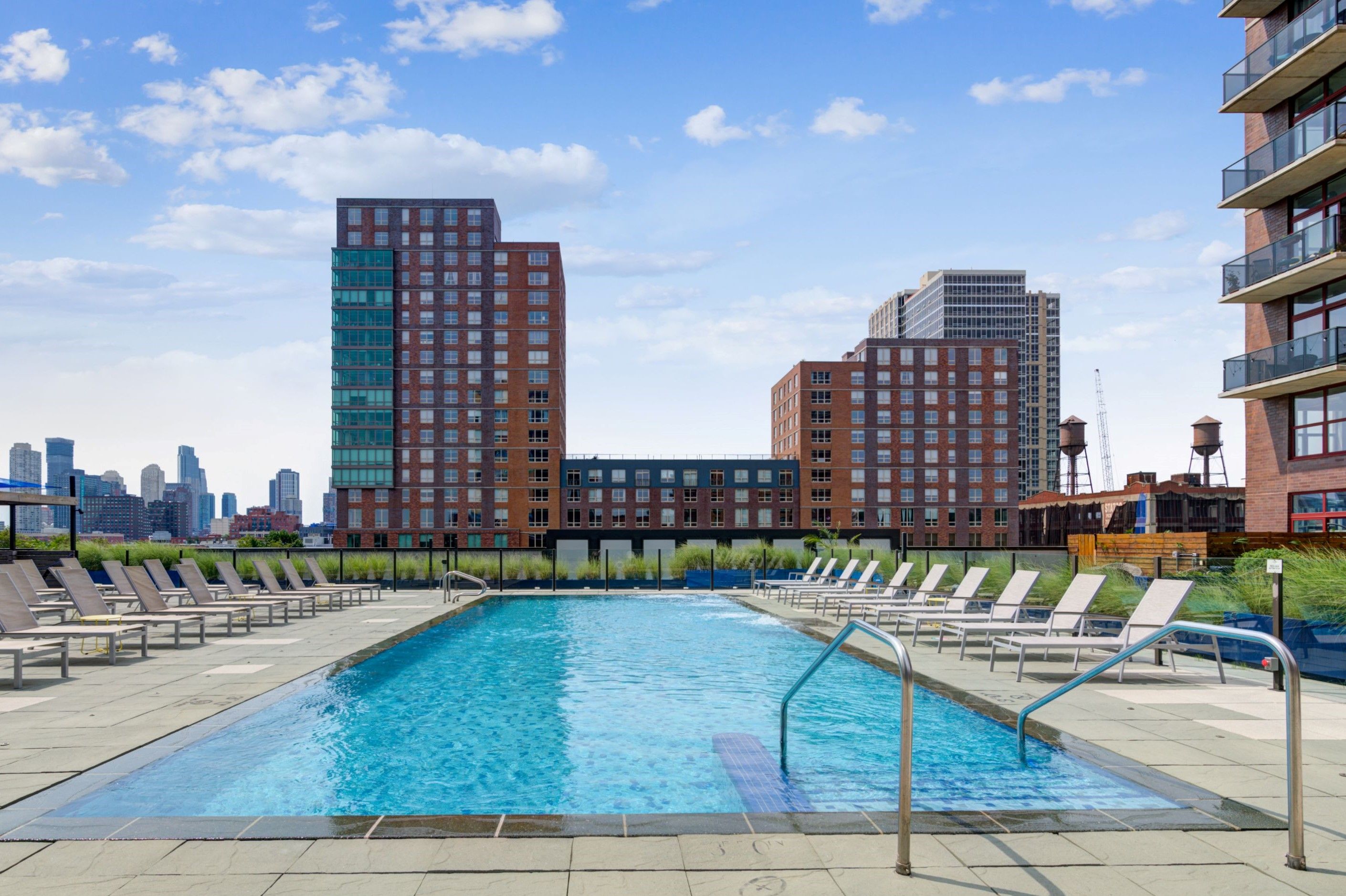 A pool surrounded by lounge chairs and buildings under a clear blue sky.