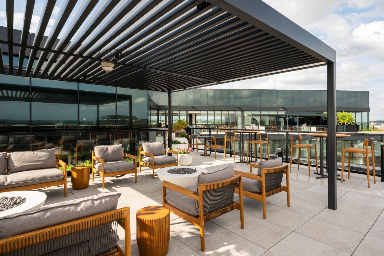 Modern rooftop terrace with seating and tables under a slatted pergola.