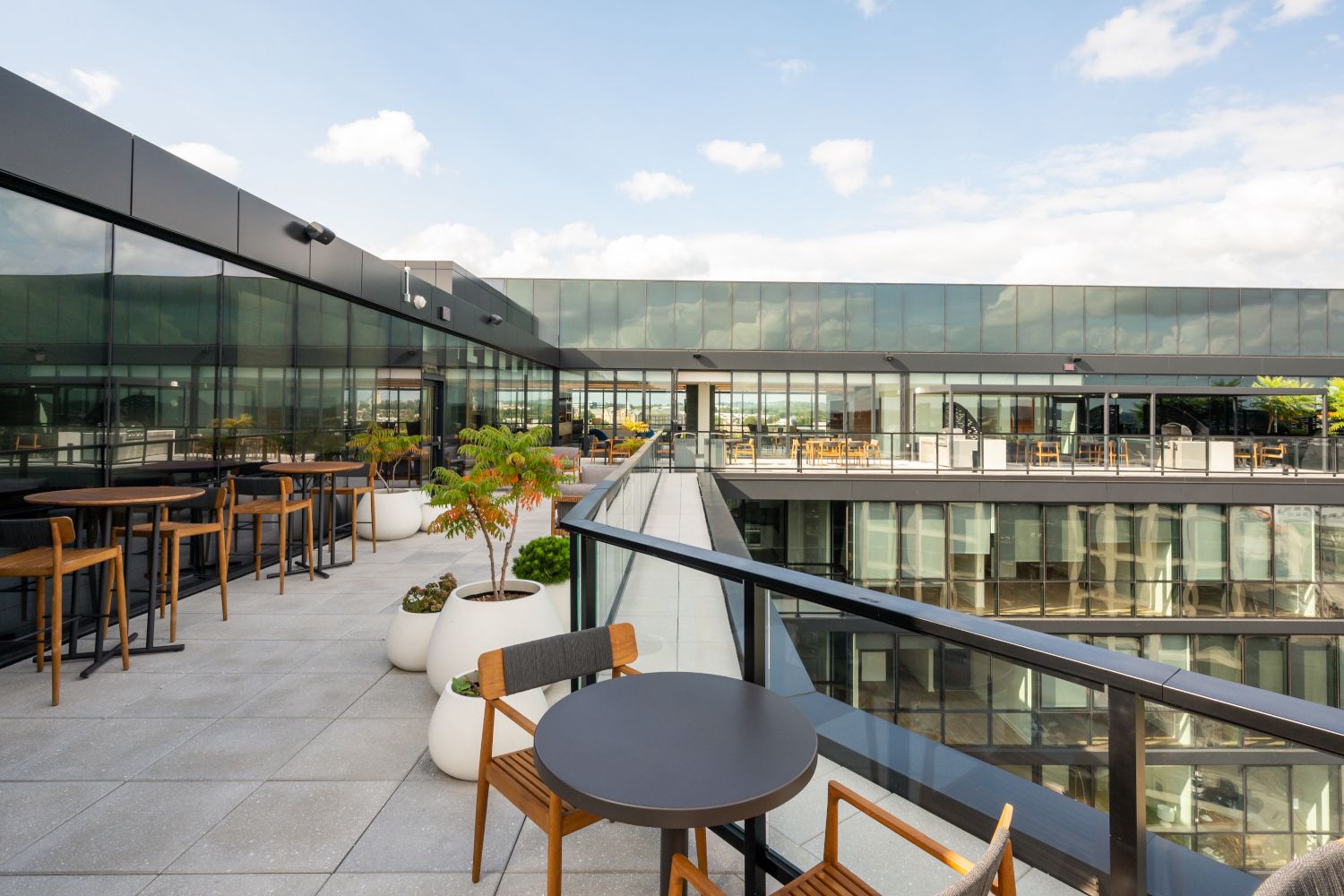 Modern rooftop terrace with tables, chairs, and glass walls against a clear sky.