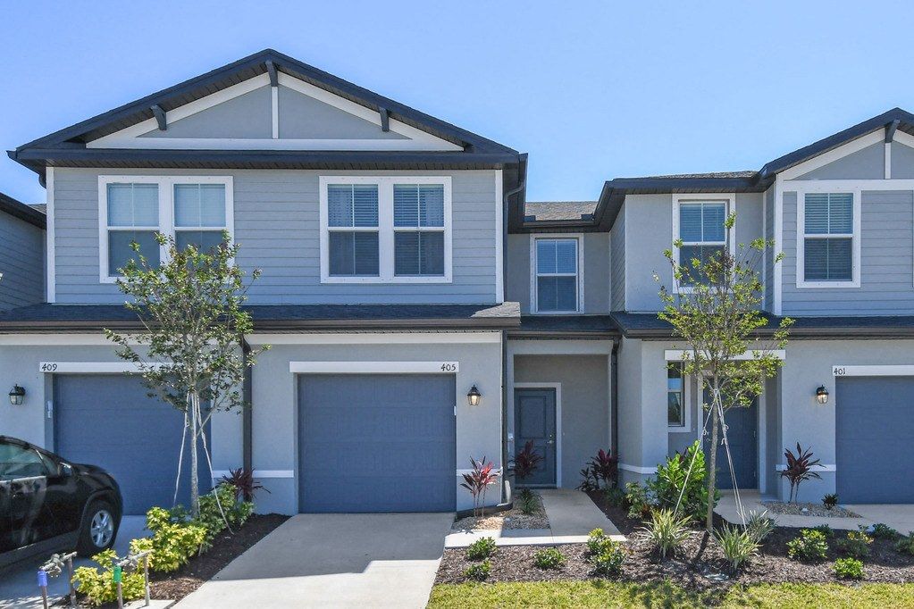 Modern townhouses with garages and landscaped front yards under a clear blue sky.