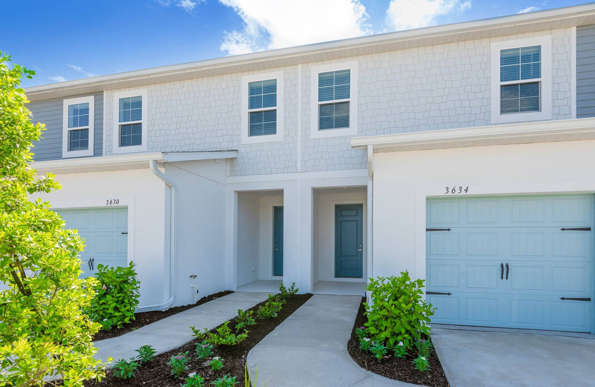 Modern two-story townhouse with light blue doors and landscaped front entrance.