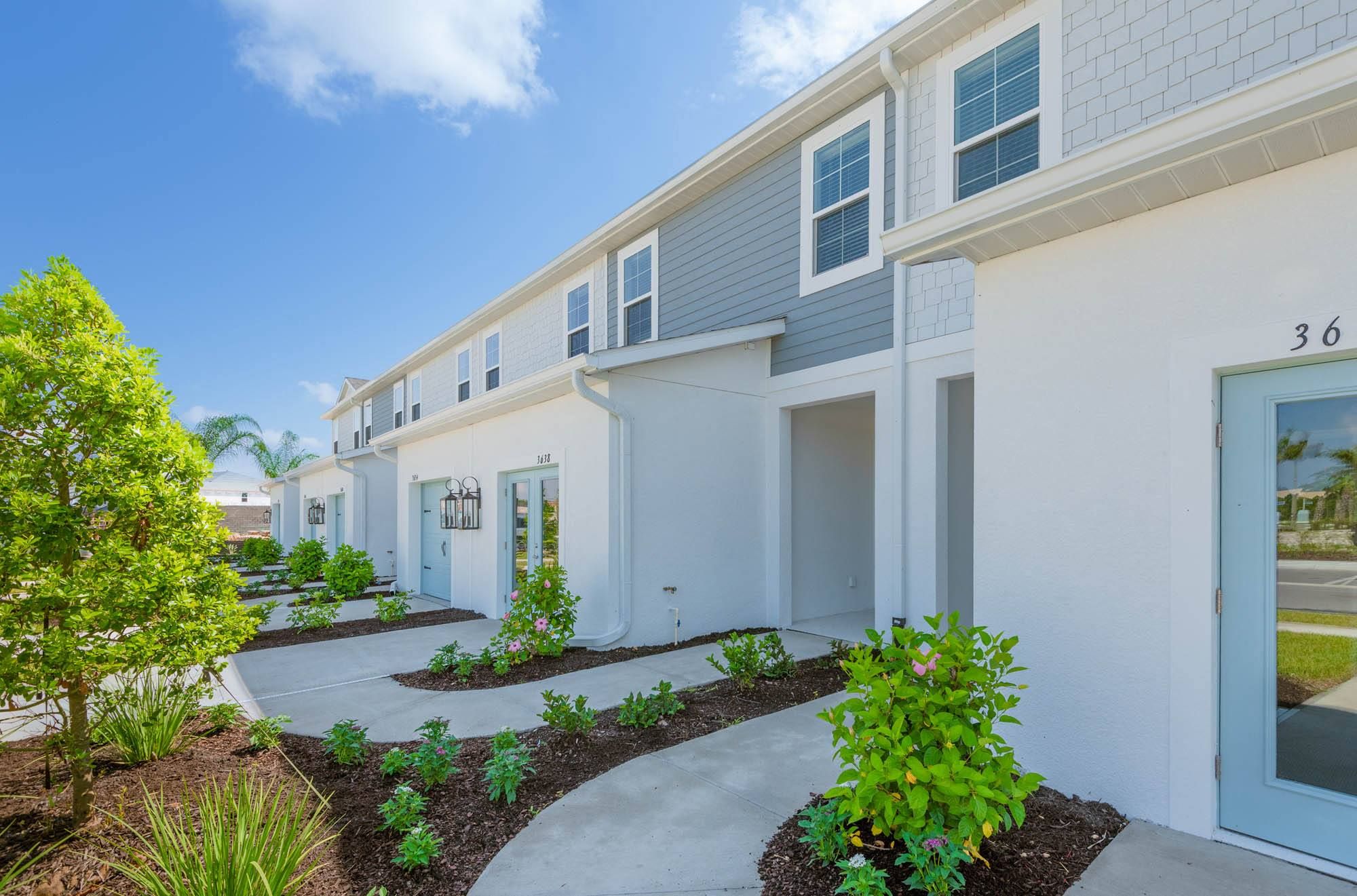 Row of modern townhouses with landscaping and a blue sky.
