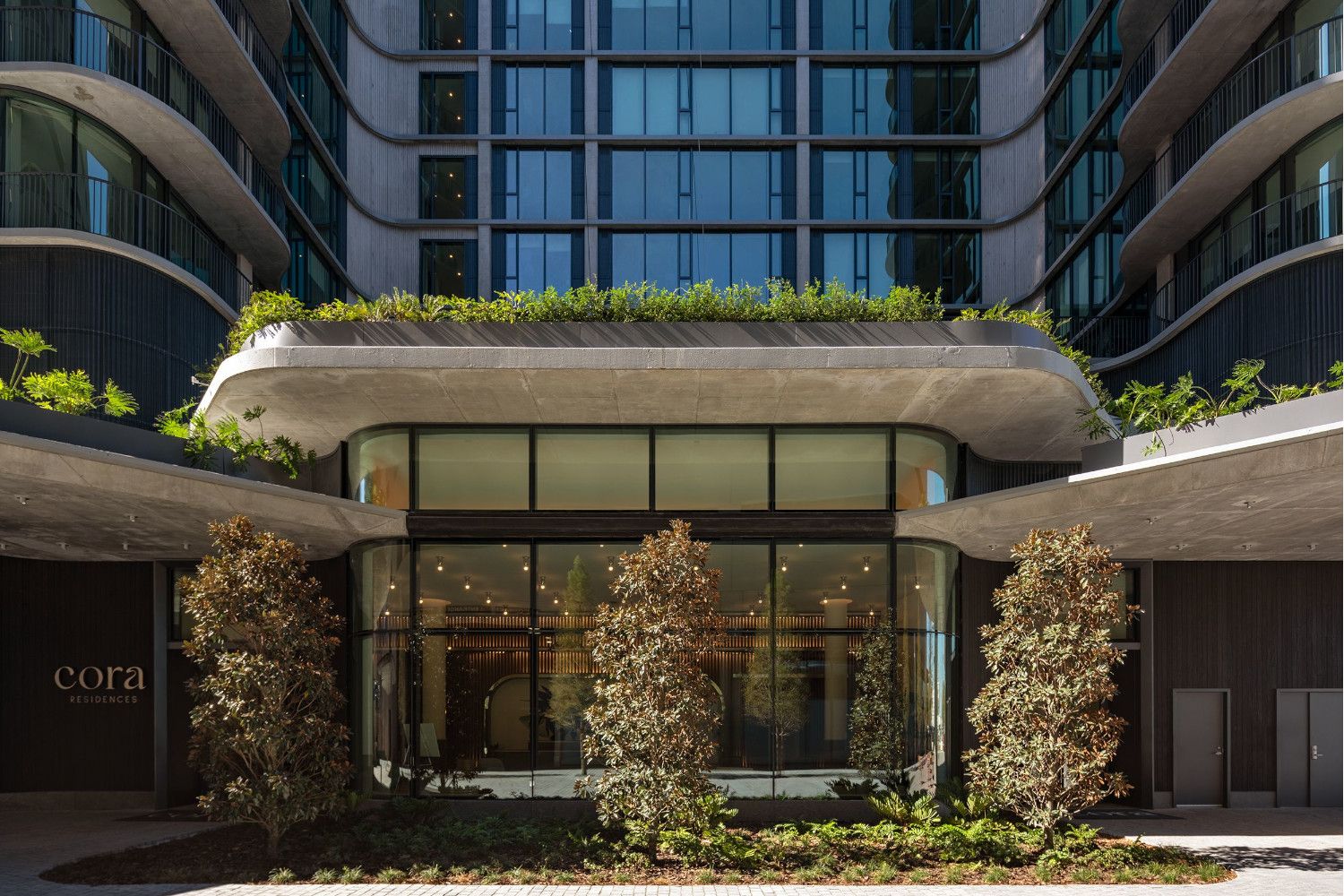 Modern building entrance with greenery and large glass windows.
