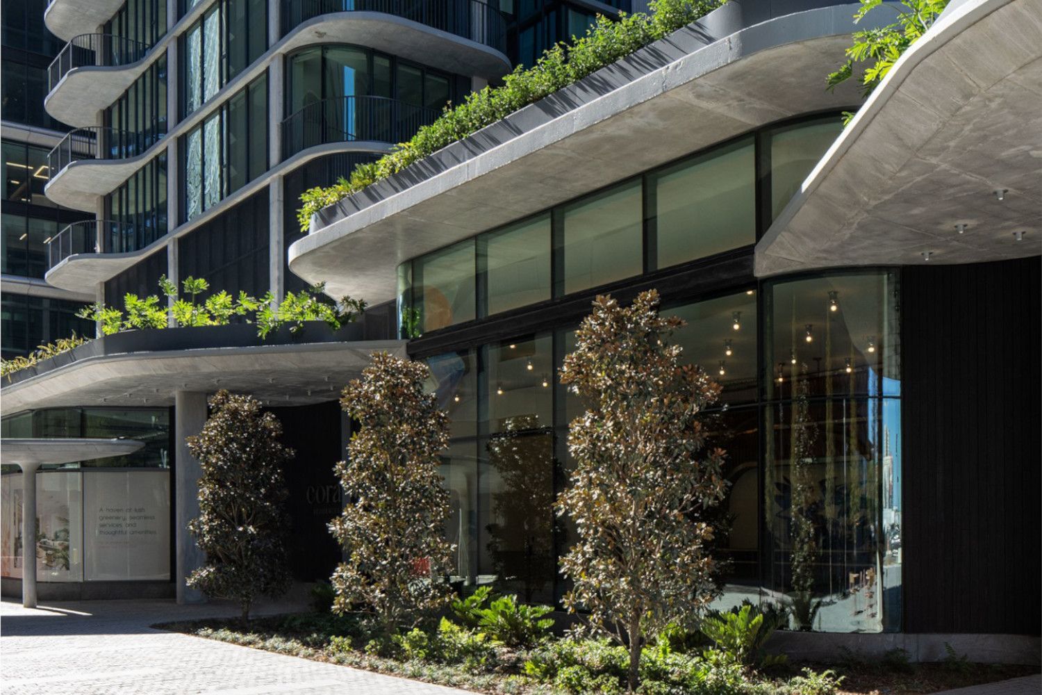 Modern building facade with large windows and greenery at the entrance.