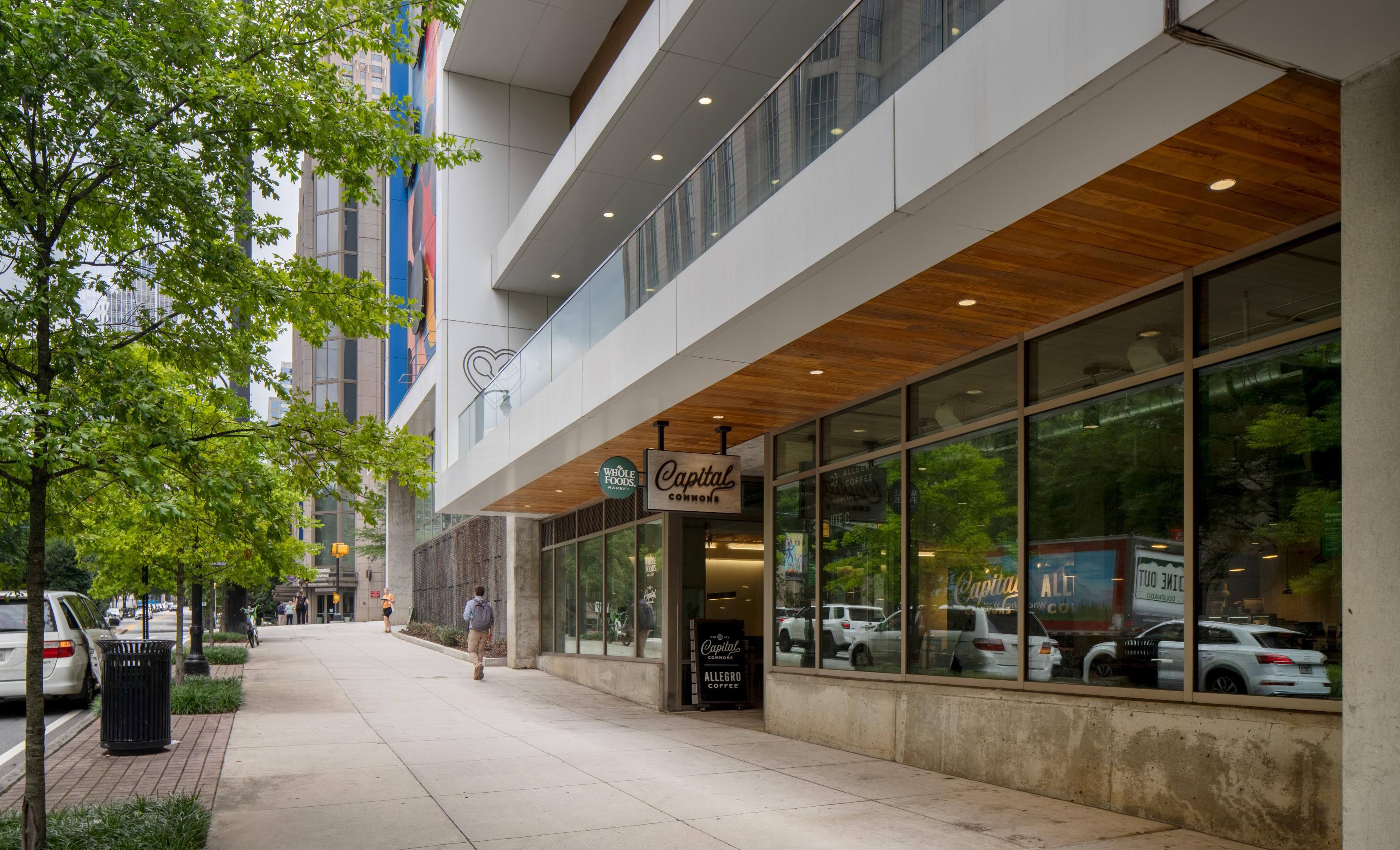 Urban scene showing a storefront with large windows and trees along the sidewalk.