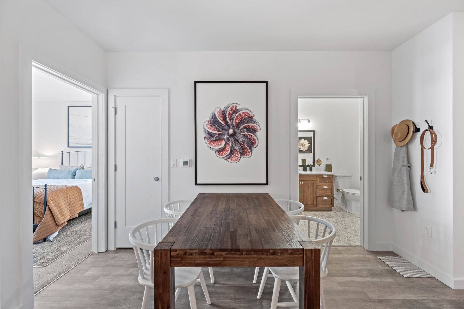 Minimalistic dining area with a wooden table, white chairs, and a colorful wall artwork.