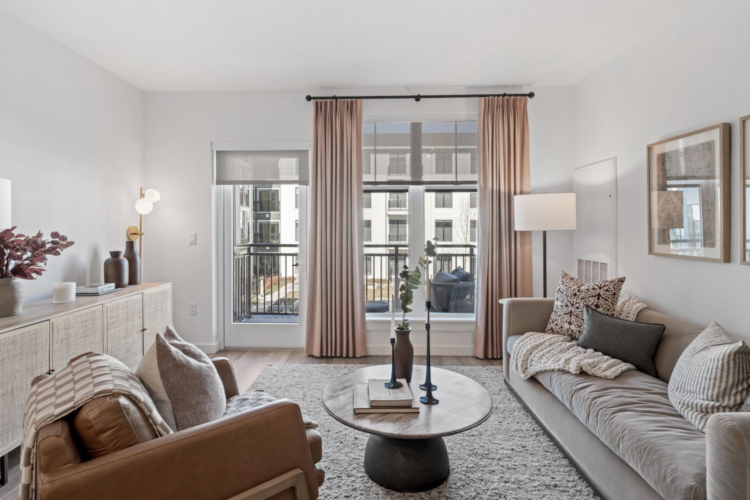 Modern living room with a soft color palette, cozy seating, and natural light from large windows.