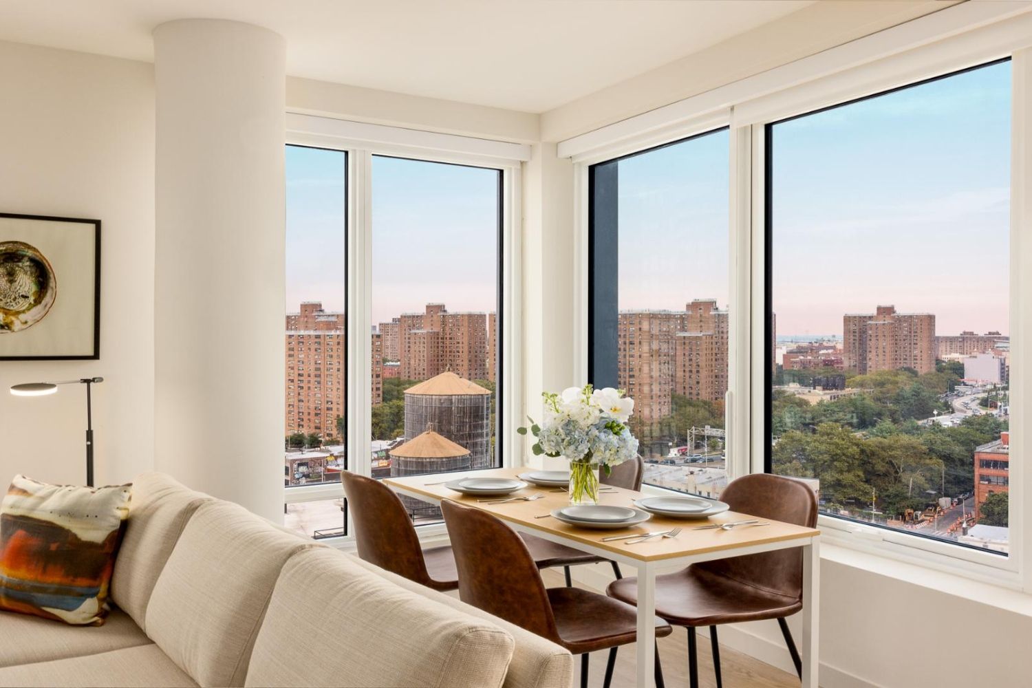 Modern living space with large windows offering city views and a dining table set with flowers.