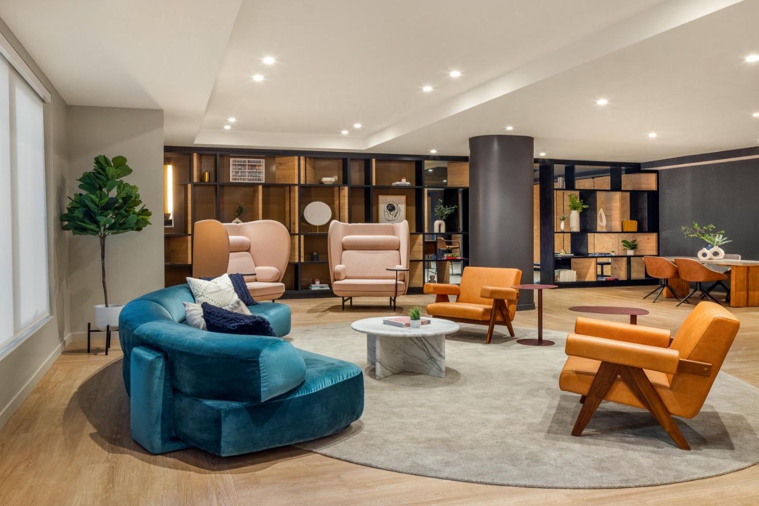 Modern lounge with colorful seating, a circular rug, and a bookshelf backdrop.