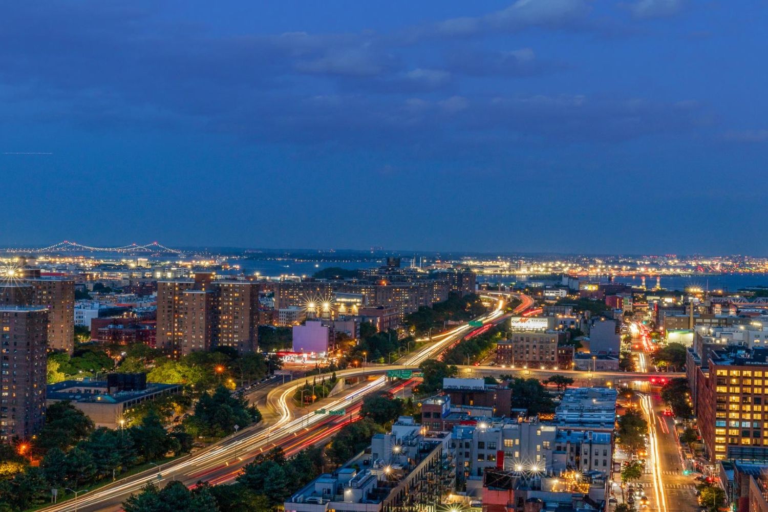 City skyline at dusk with lights and a winding road.
