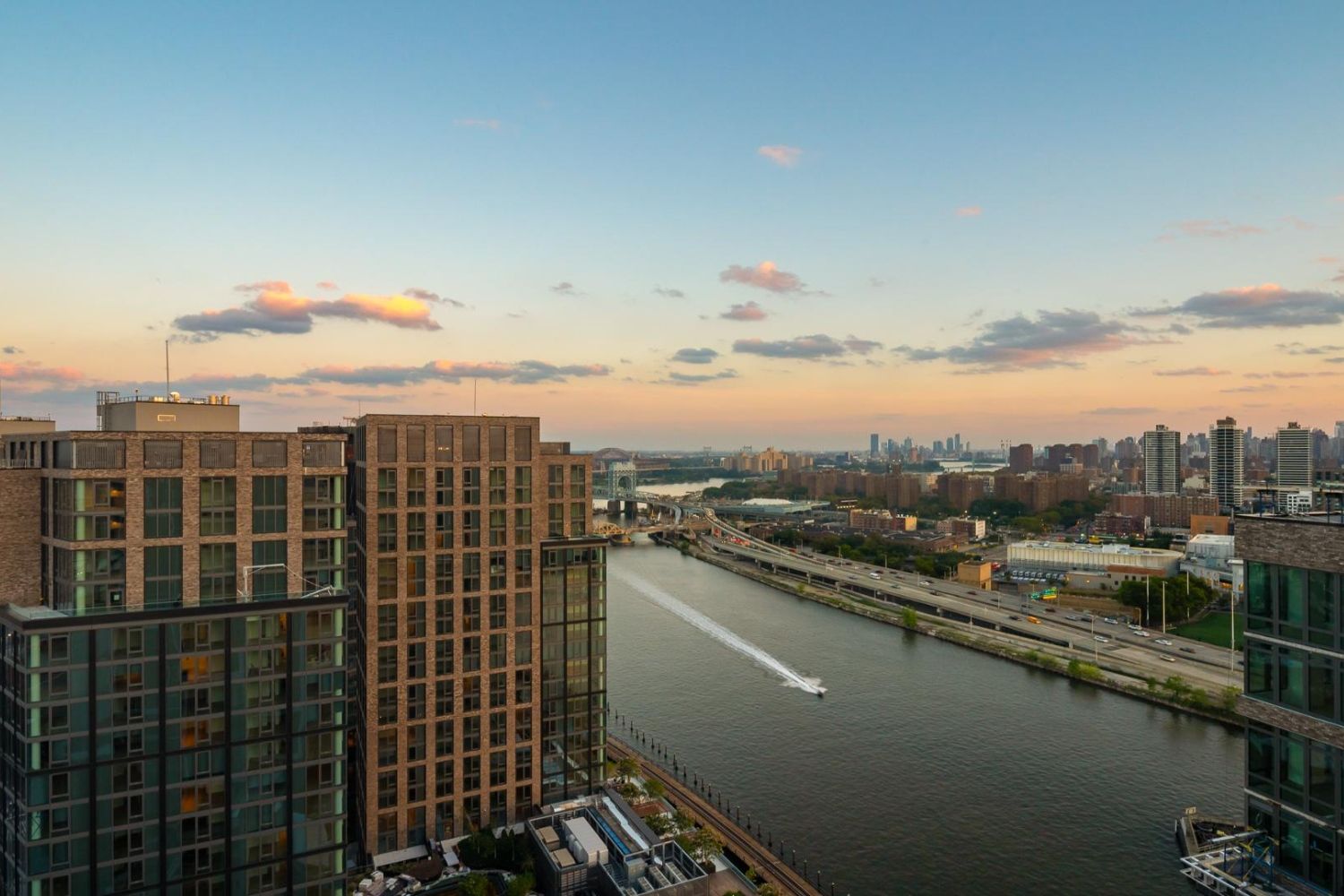 City skyline at sunset with a river and a boat in the foreground.