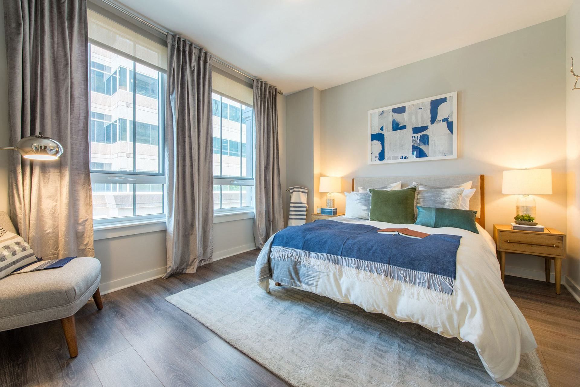 Cozy bedroom with a blue and white bedspread, armchair, and large windows.