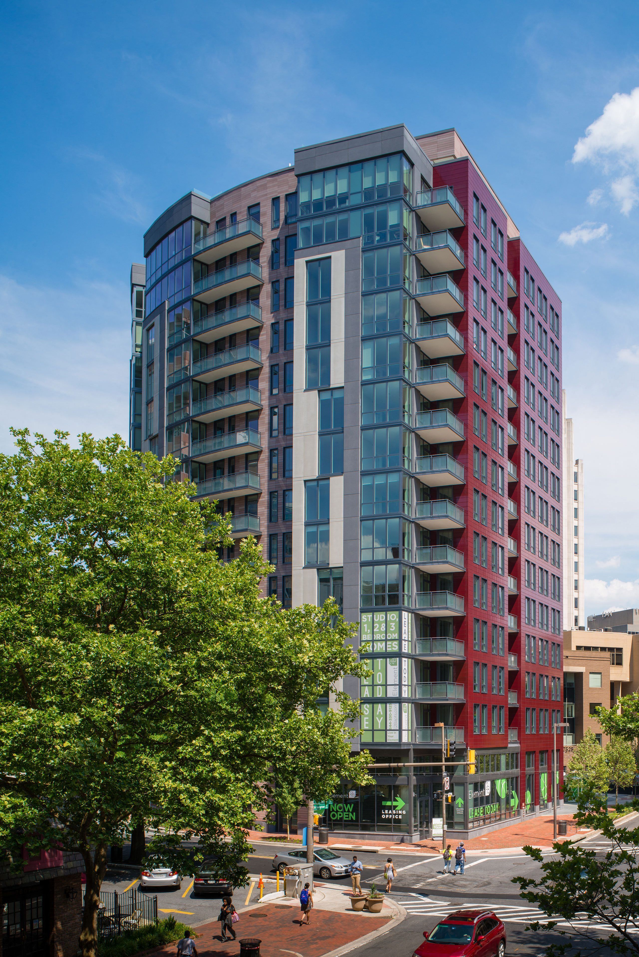 Modern multi-story building with a glass facade and greenery in the foreground.