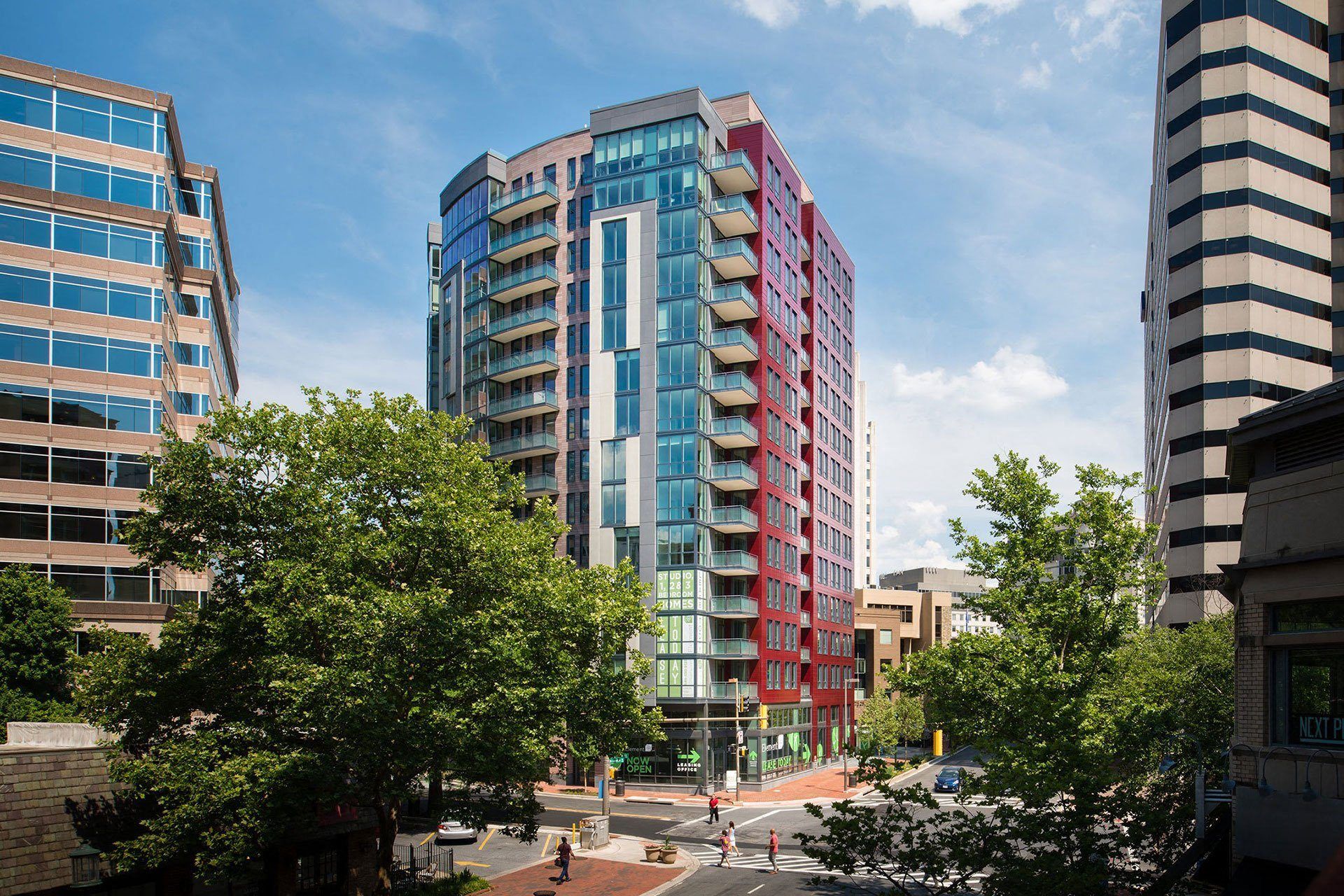 Modern skyscraper surrounded by urban greenery under a blue sky.