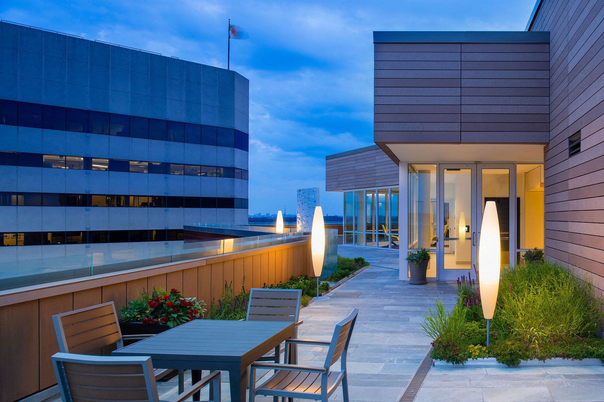 Modern rooftop terrace with tables, chairs, and ambient lighting at dusk.