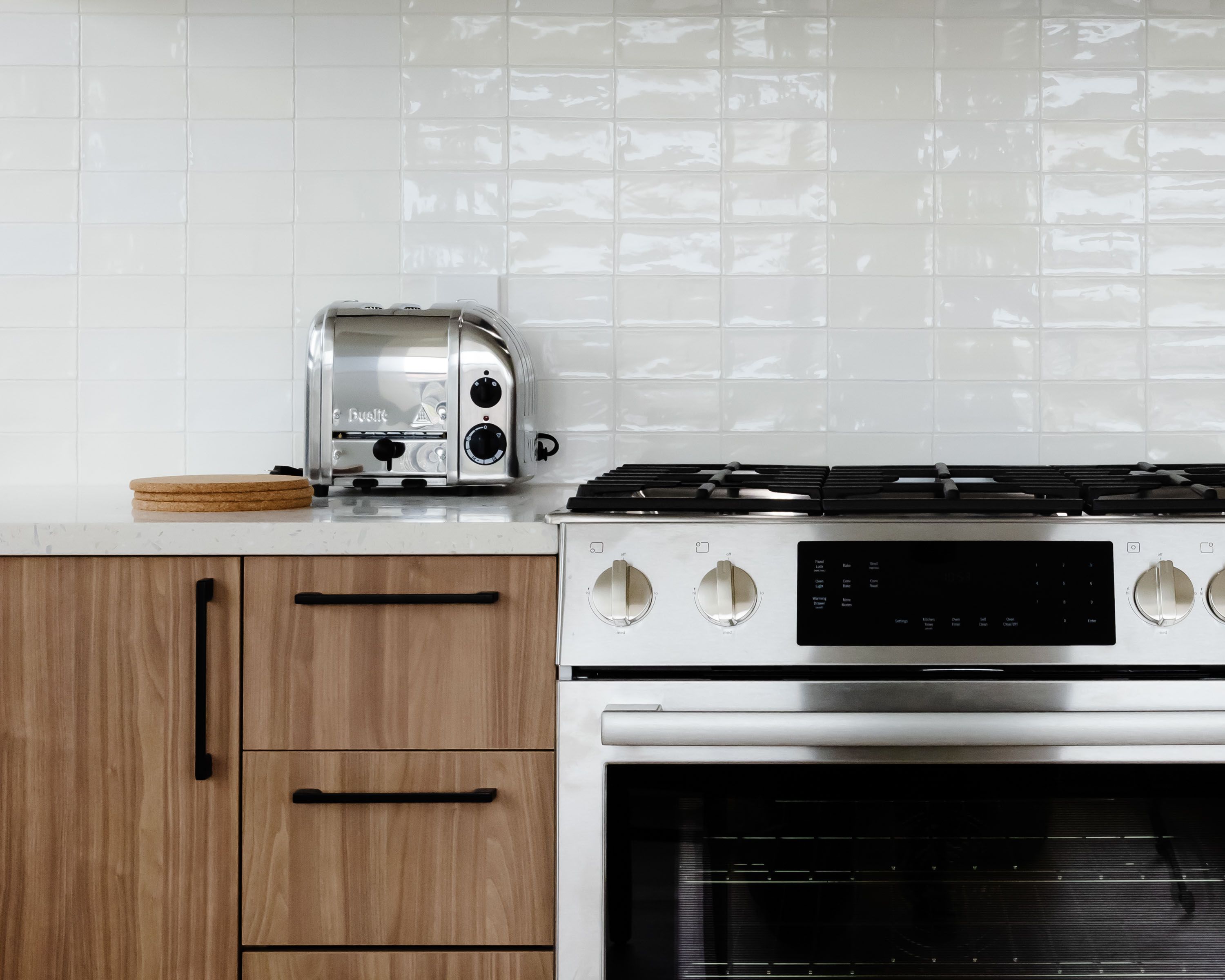 Modern kitchen scene featuring a toaster and a gas stove against a white backsplash.