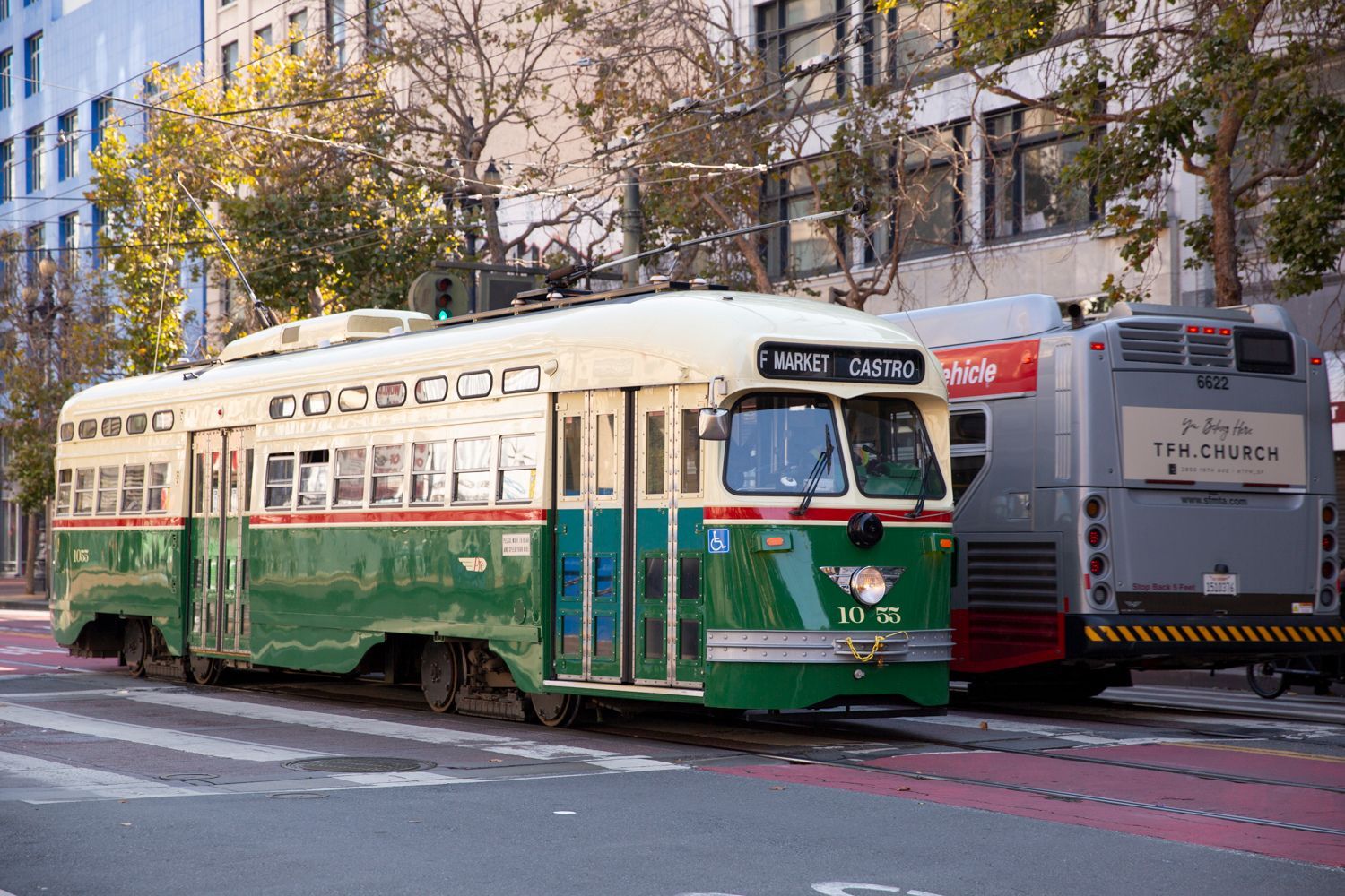 Vintage green and cream tram on a city street near a parked bus.