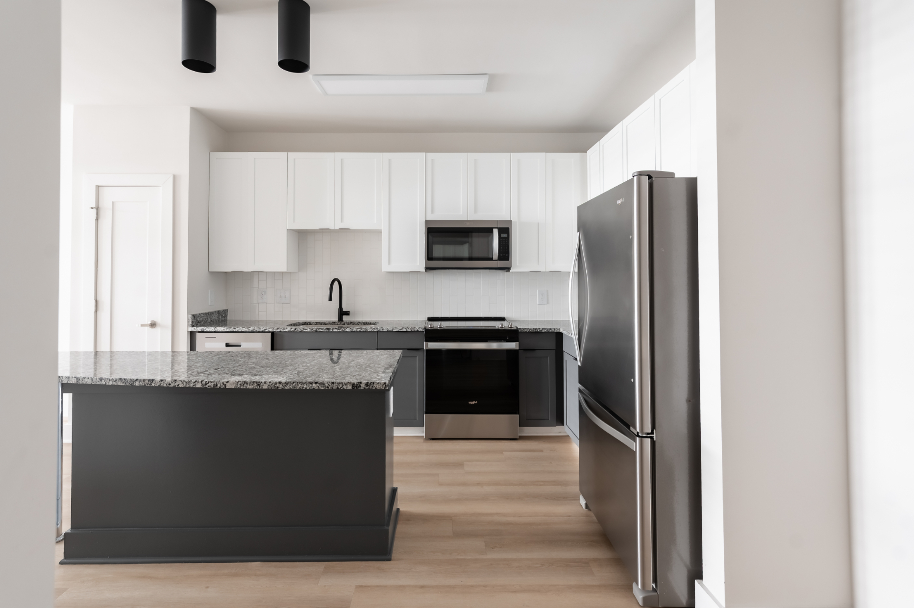 Modern kitchen with gray island, white cabinets, and stainless steel appliances.