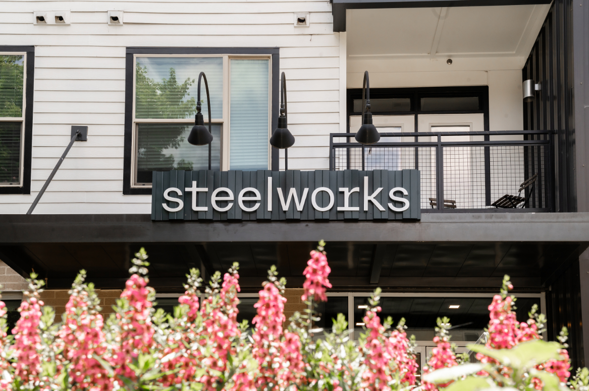 Sign reading 'steelworks' above pink flowers in front of a building.