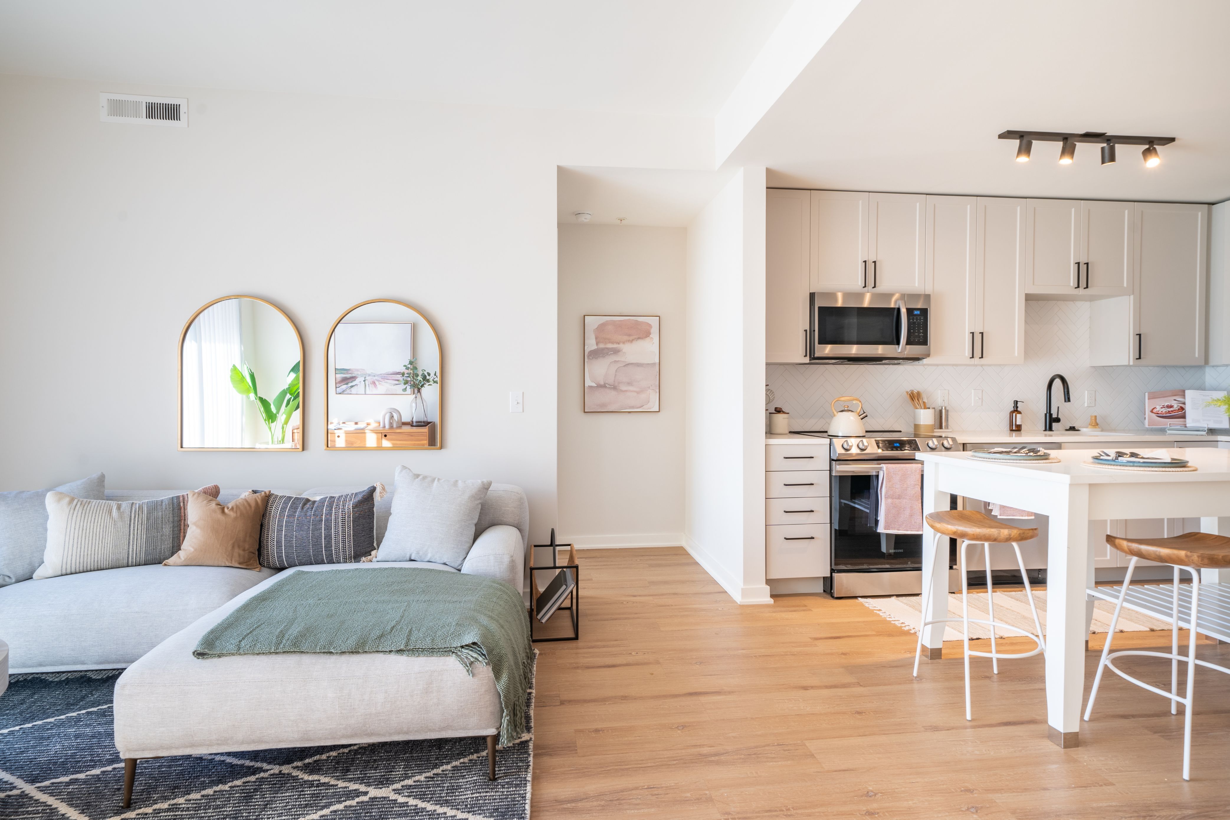 Bright, modern open-concept living space with a sofa, kitchen, and decorative mirrors.