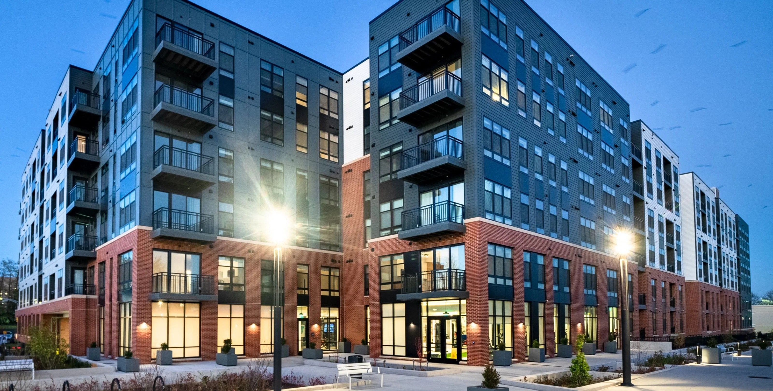 Modern multi-story apartment building with balconies and street lighting at dusk.