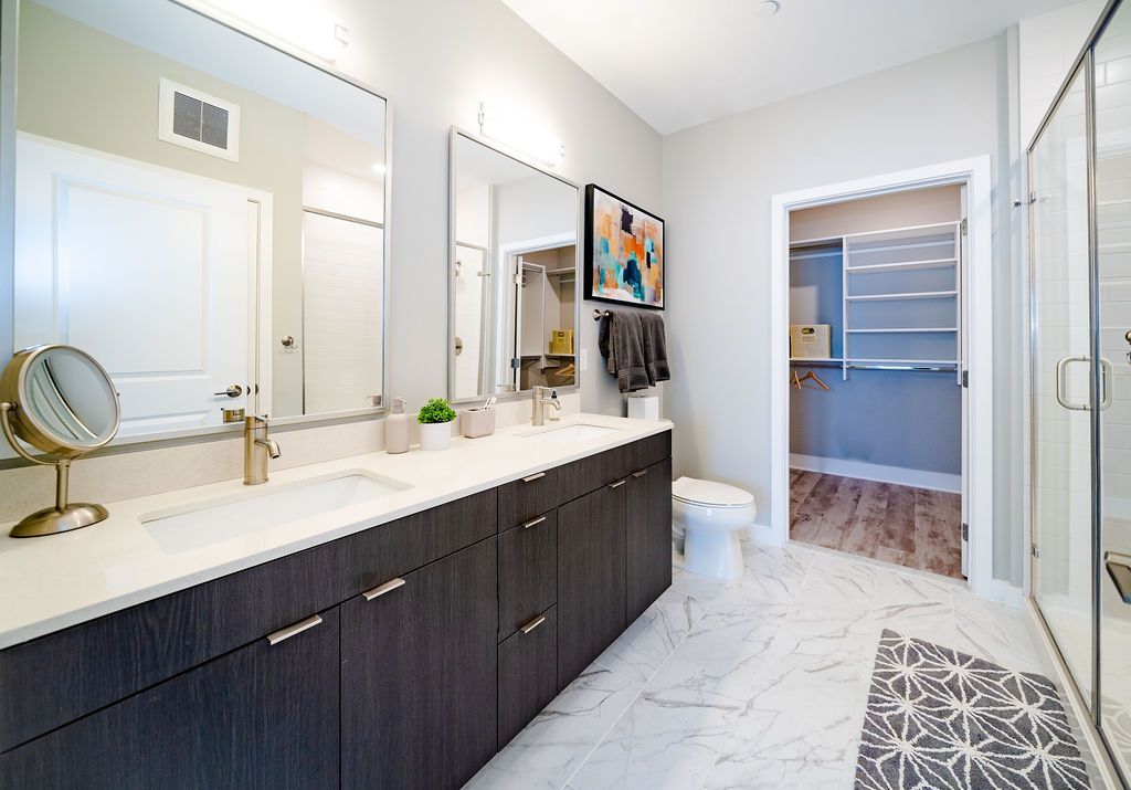 Modern bathroom with dual sinks, mirrors, and a walk-in shower, featuring neutral tones.