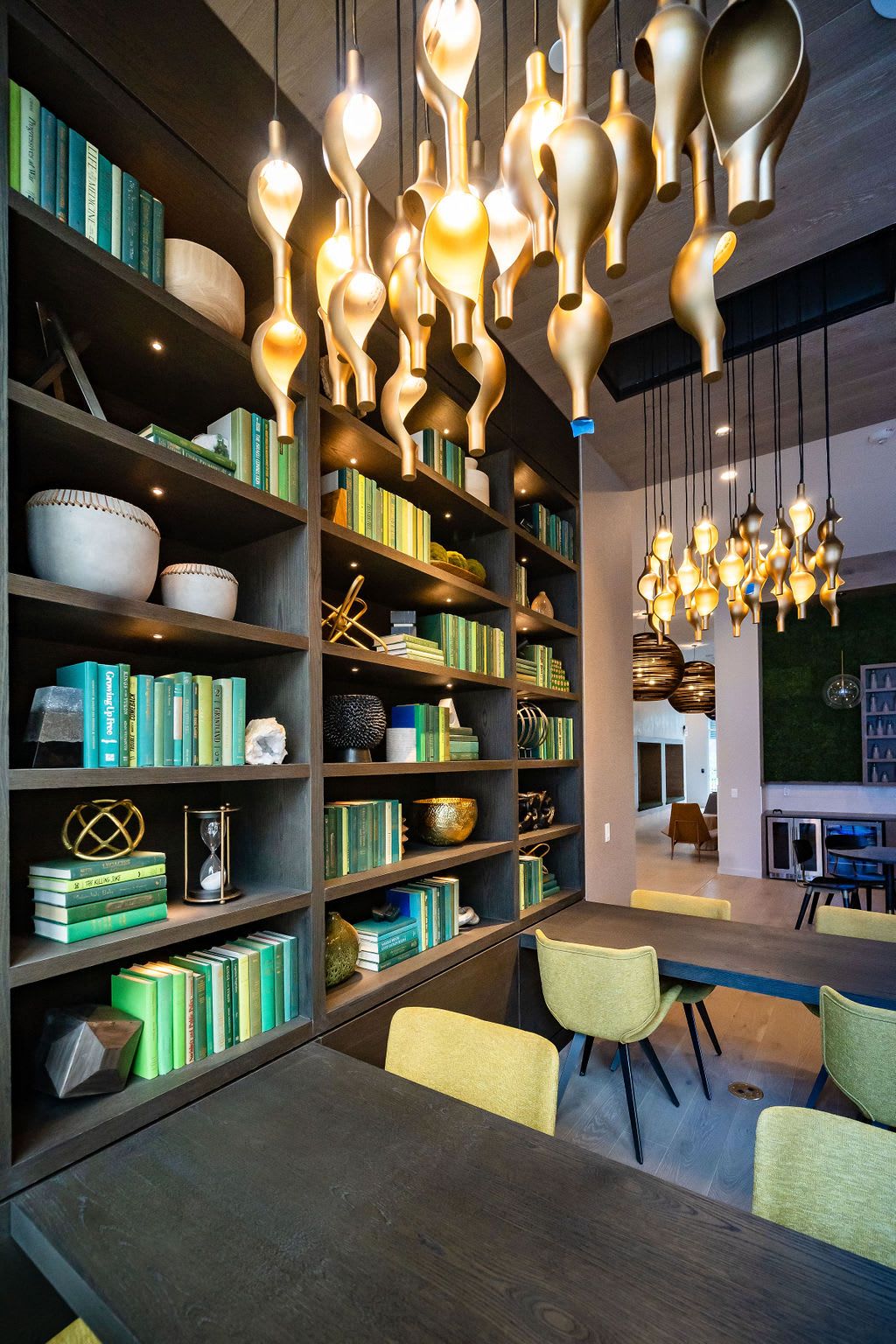 Modern interior with lit shelves, green books, and unique pendant lights.