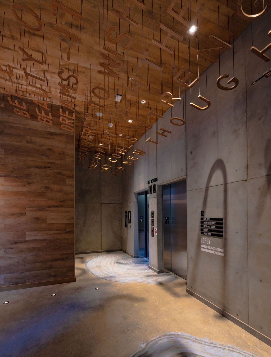 Modern elevator lobby with wood and concrete walls, illuminated by stylish ceiling fixtures.