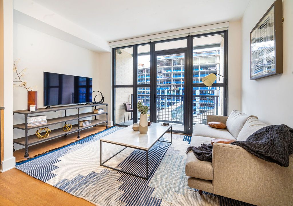 Modern living room with a sofa, coffee table, TV, and large windows showing a city view.