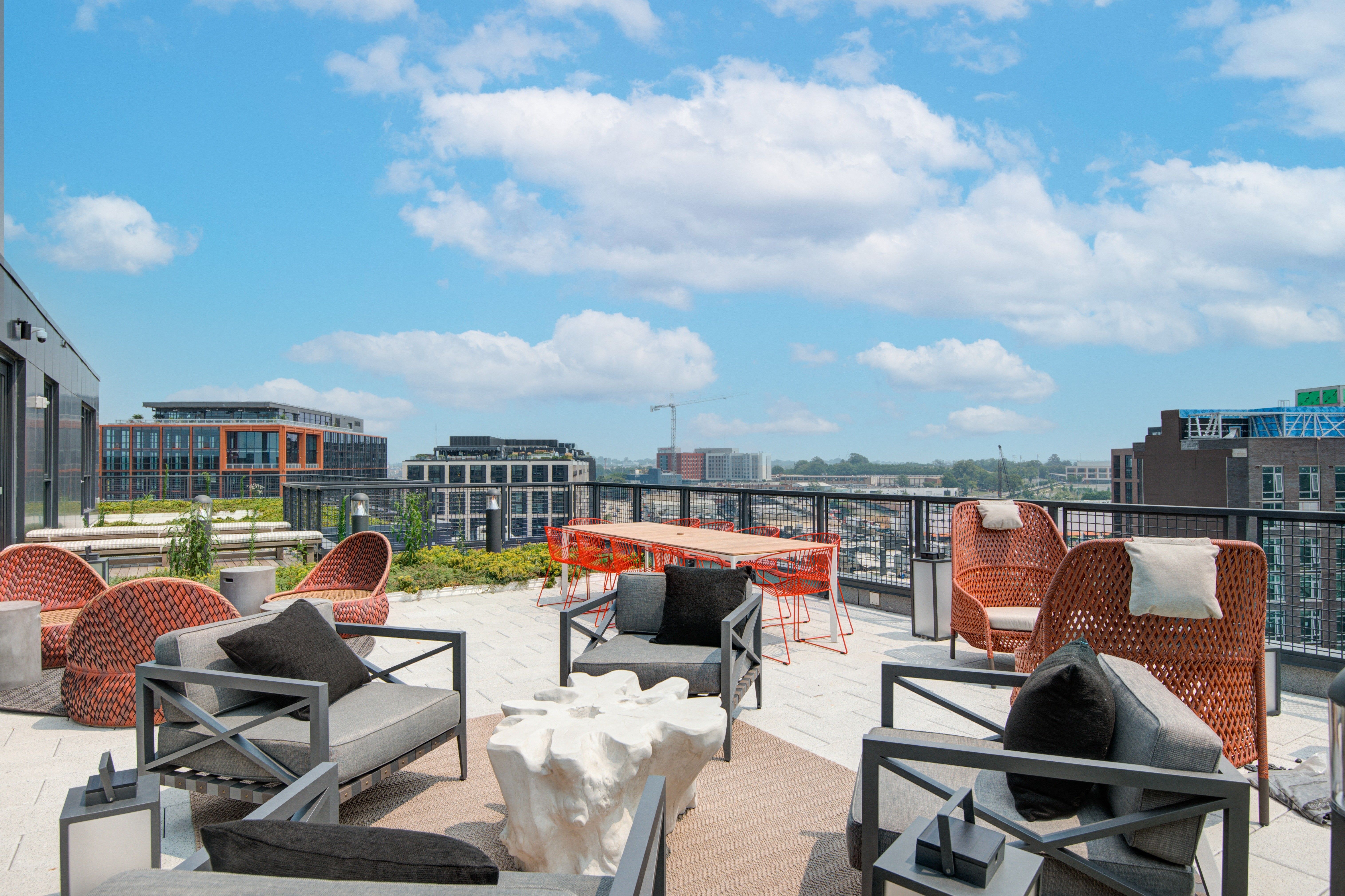 Modern rooftop terrace with seating, overlooking a city skyline and blue sky.