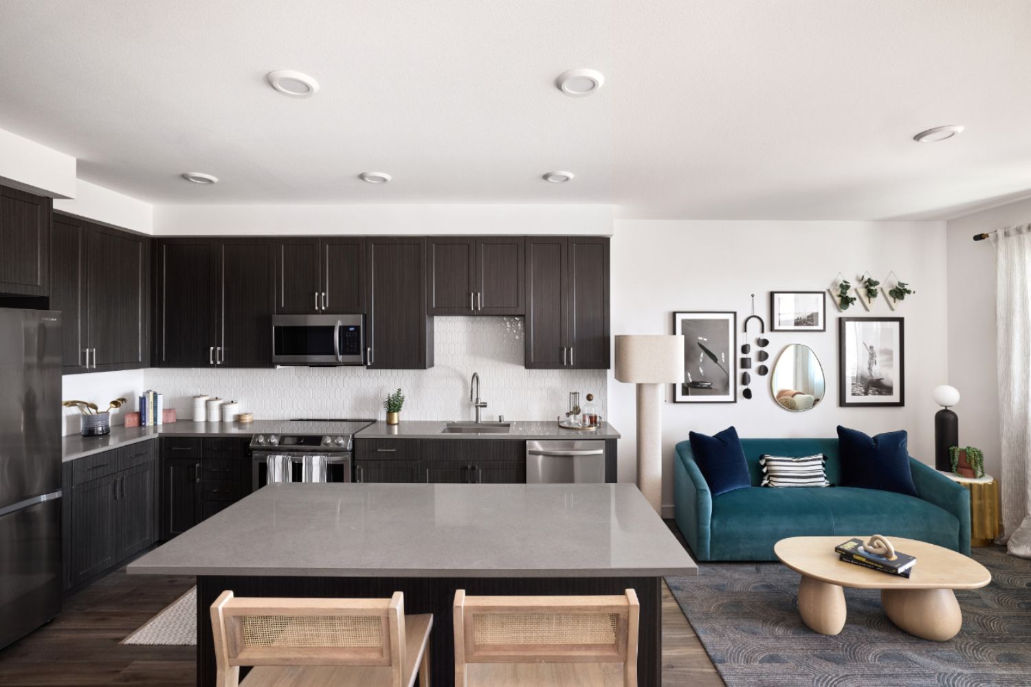 Modern kitchen and dining area with dark cabinetry and a cozy teal sofa.