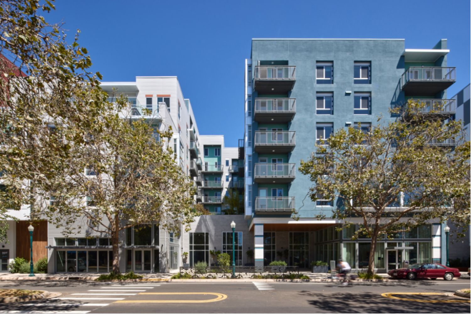 Modern apartment buildings with balconies and trees in front under a clear blue sky.