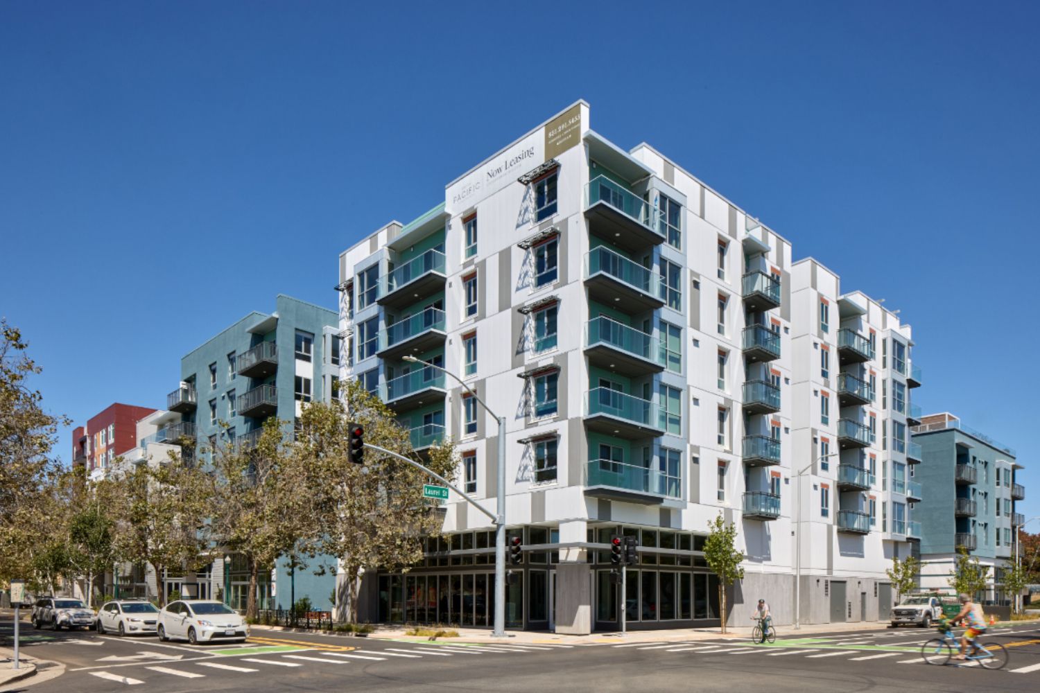 Modern apartment building at a street intersection under a clear blue sky.
