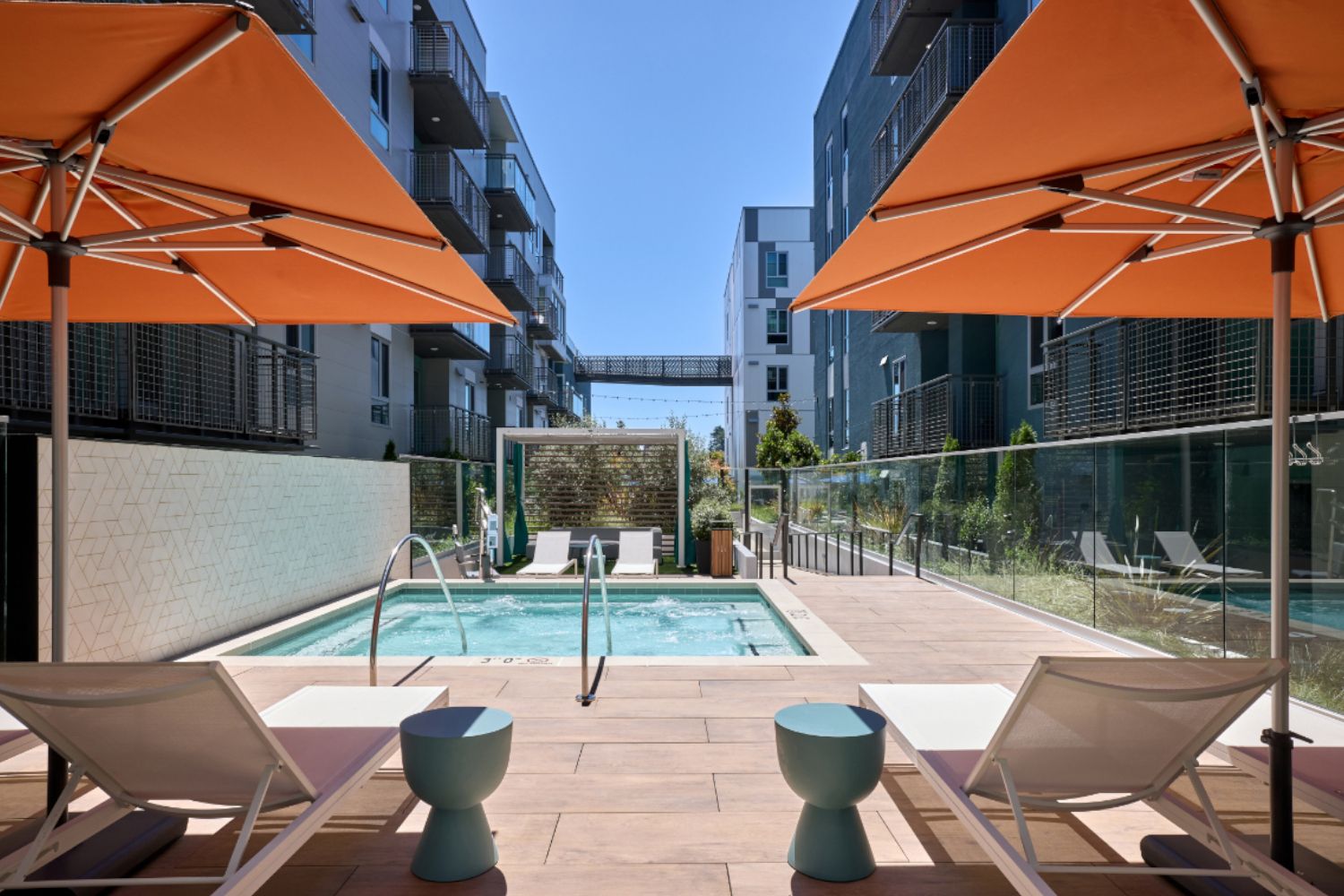 Poolside view with orange umbrellas and modern apartment buildings in the background.