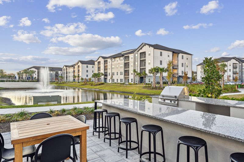 Modern apartment buildings by a pond with outdoor seating and a barbecue area.
