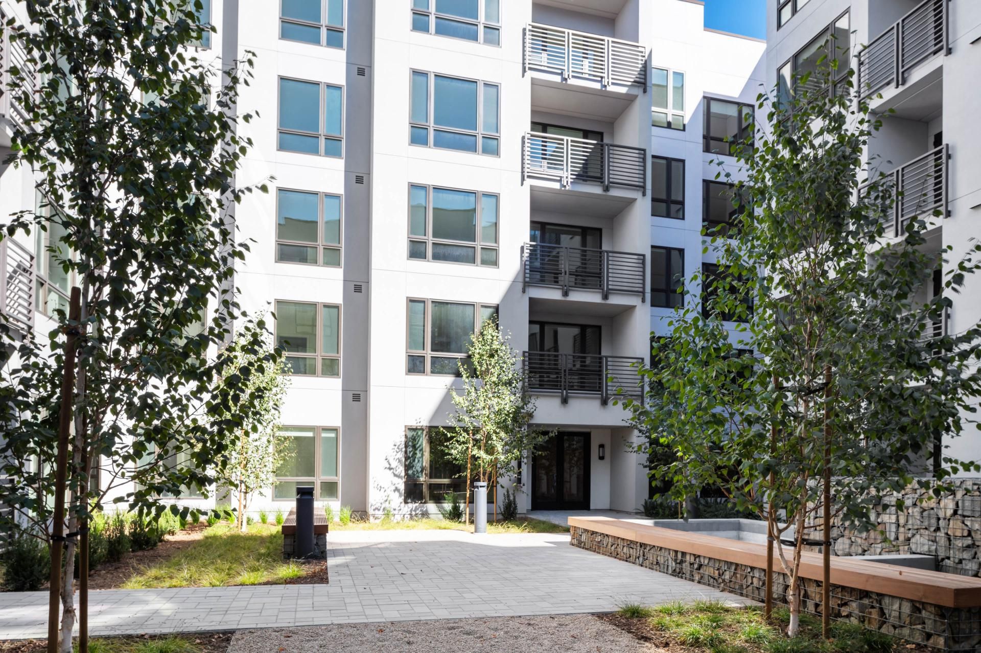 Modern apartment complex courtyard with greenery and seating areas.